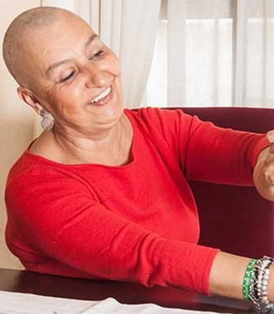 A bald woman smiles as she adjusts a wig on a wig stand