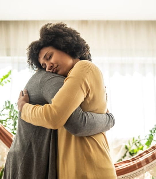 Two people embracing in a bright room with plants