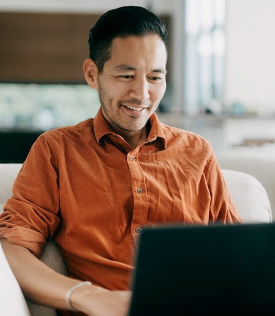 A person wearing an orange shirt looks down at a computer screen.