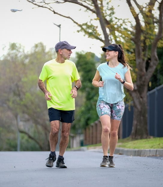 A woman and man smile while running outside