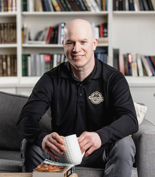 A smiling man sitting on a sofa holding a coffee cup in his hands.