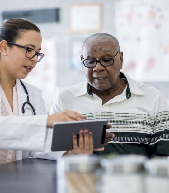 An older man reviewing test results on a tablet with a female doctor.