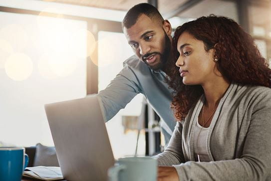 Un couple assis à une table qui regarde un ordinateur portable.