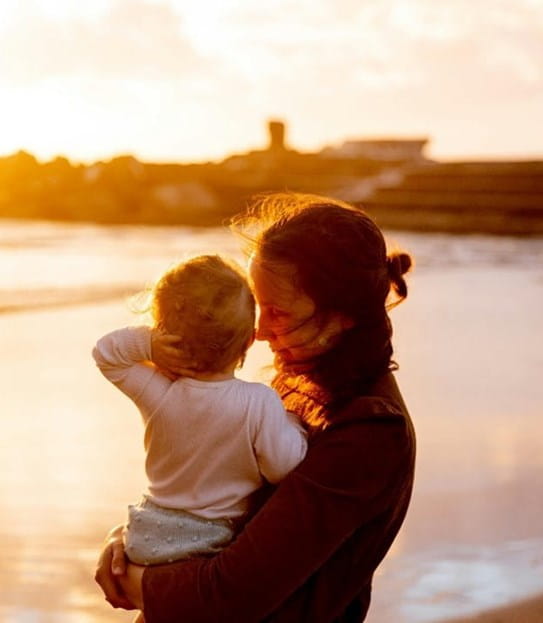 A person holding a child on a beach.