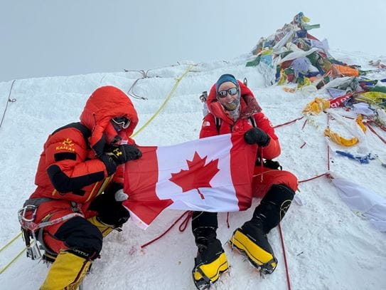 Meredith et une autre personne, assises dans la neige en  tenant un drapeau canadien