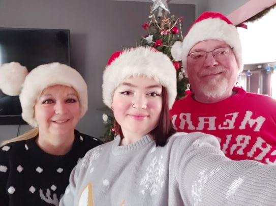 Hailey and her parents smiling at the camera and wearing Santa hats.