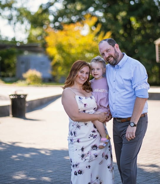Natalie Lipschultz, carrying her daughter, stands next to her husband in a park.