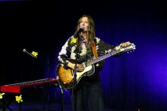 BEYRIES standing on a stage holding a guitar and singing into a microphone.
