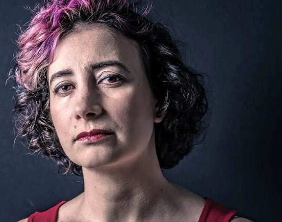 Une femme dans la quarantaine, à l’expression sérieuse, établit un contact visuel.