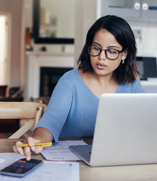 A woman is sitting in front of a laptop and using a calculator