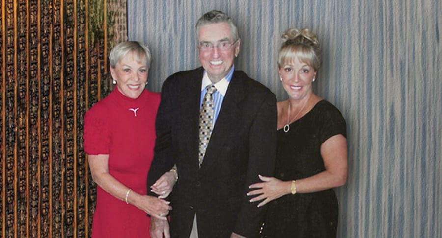 Three people in formal clothing standing together smiling.
